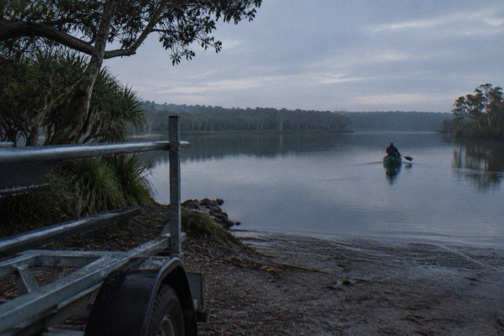 Calm dark water of a lake at dawn with forested shoreline in the distance