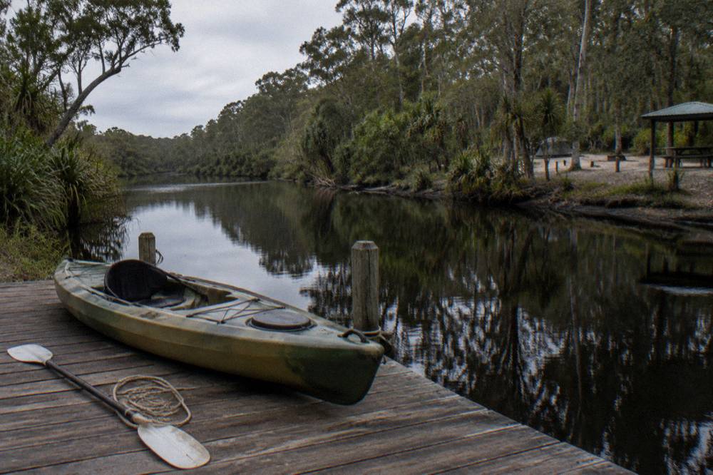A kayak resting on a wooden jetty above dark reflective river water