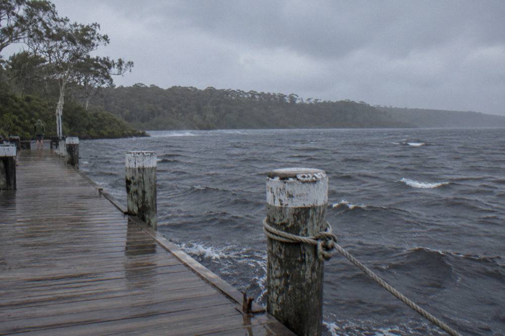 Calm dark water at a jetty on Lake Cootharaba with forest on the far shore