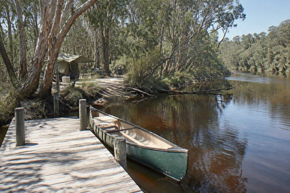 A timber jetty extending over calm dark river water with canoe moored nearby