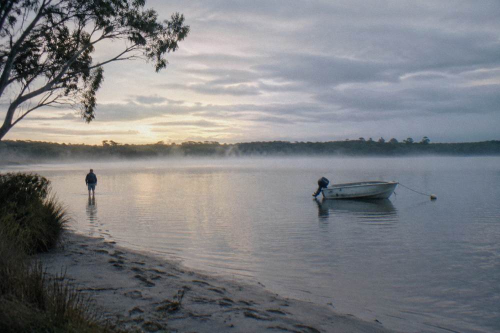 Wide calm lake at dawn with mist over the water and distant treeline