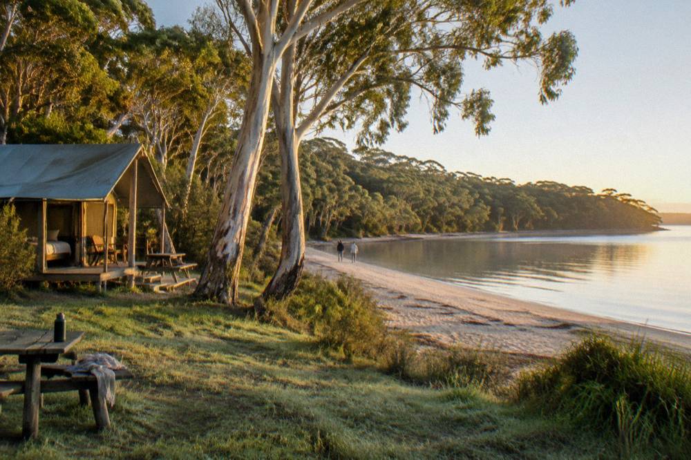 Wide sandy beach with low headland at one end and calm morning water