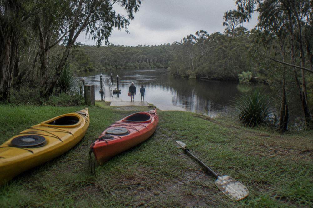 Kayaks resting on a grassy bank beside dark river water at a canoe launch point