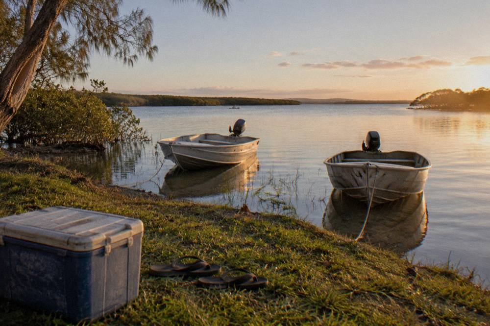 Grassy lake shore at Boreen Point with calm tea coloured water and moored small boats