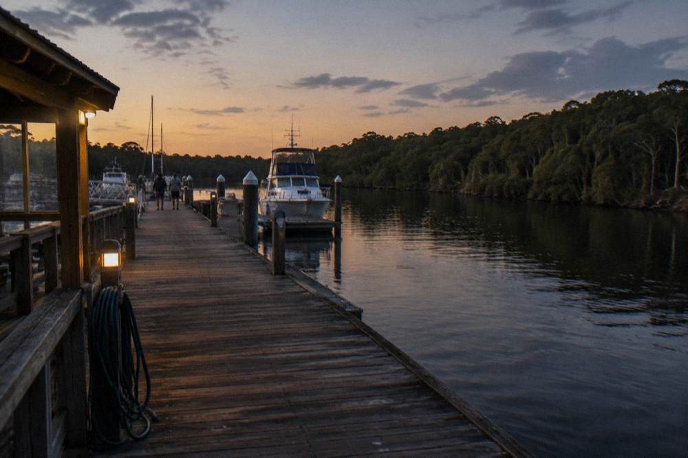 Timber jetty extending over dark calm water with forest on the far bank