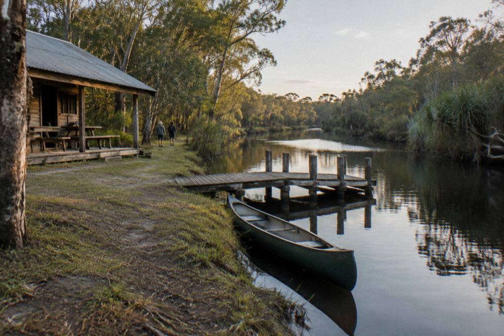 A single canoe on still dark water near a timber jetty in morning light
