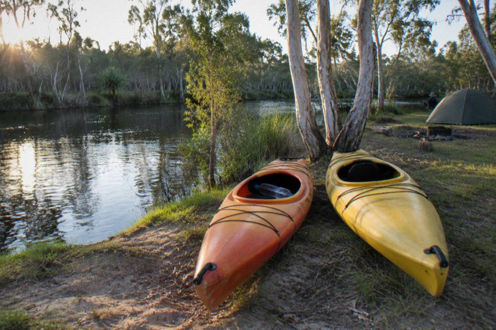 Kayaks pulled up on a grassy bank beside a calm dark river in late afternoon light