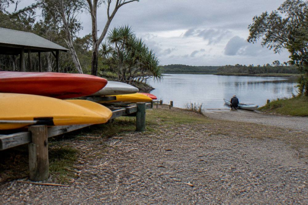 A gravel launch area beside a lake with kayaks stacked near the water