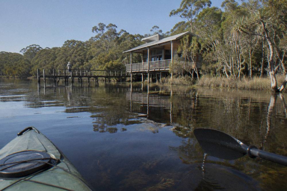 Calm dark water of a shallow lake with a wooden boardwalk information centre at the forested shoreline