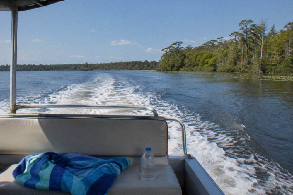 Small open cruise boat moving across a wide calm lake toward a distant green shoreline
