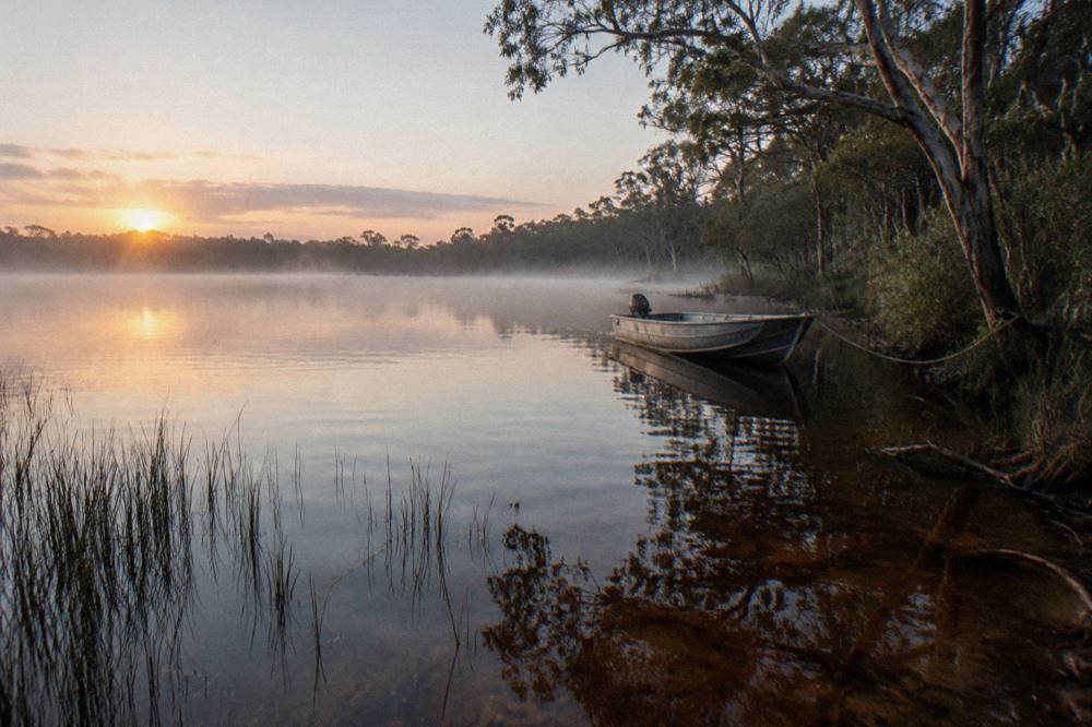 Open lake at first light with mist over dark water and a pale sunrise sky