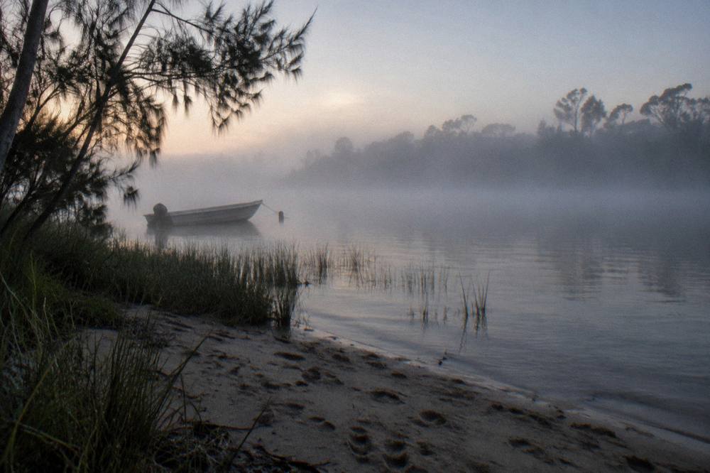 Morning mist over a wide calm lake with dark water and distant forest at dawn