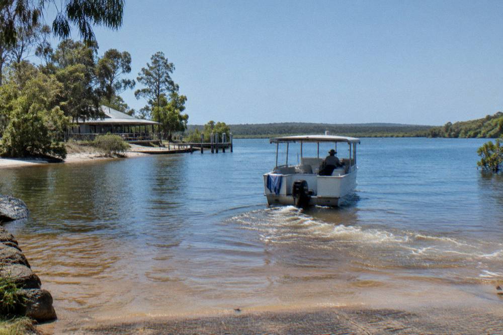 Cruise boat moving slowly along a narrow reflective river between trees