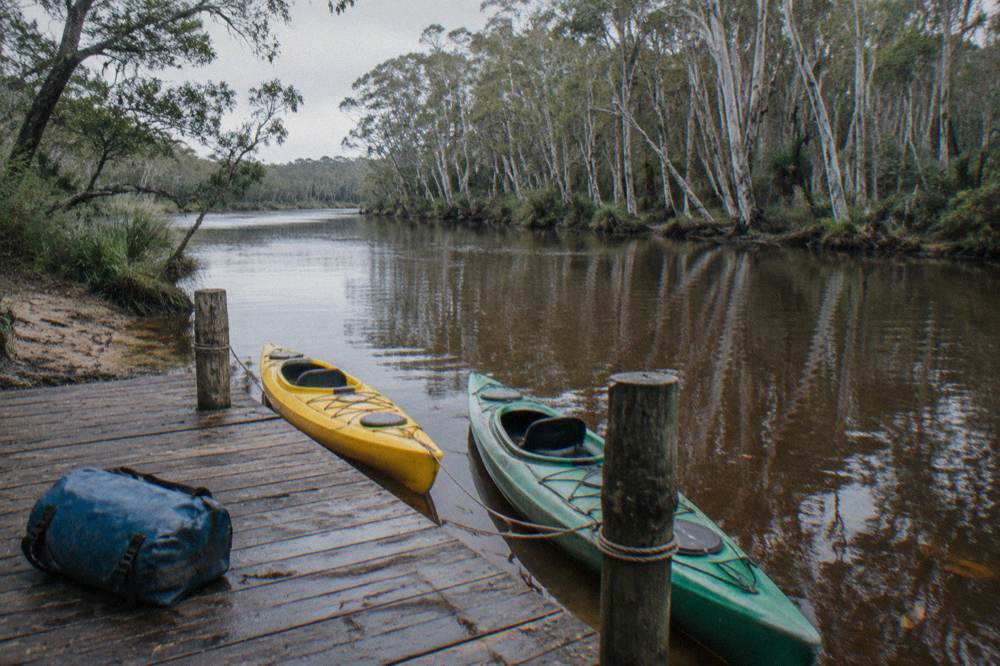 two kayaks tied at a timber jetty on a narrow brown river