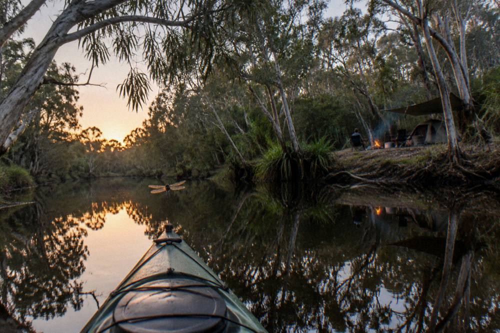 a kayak gliding through narrow still water reflecting overhanging trees