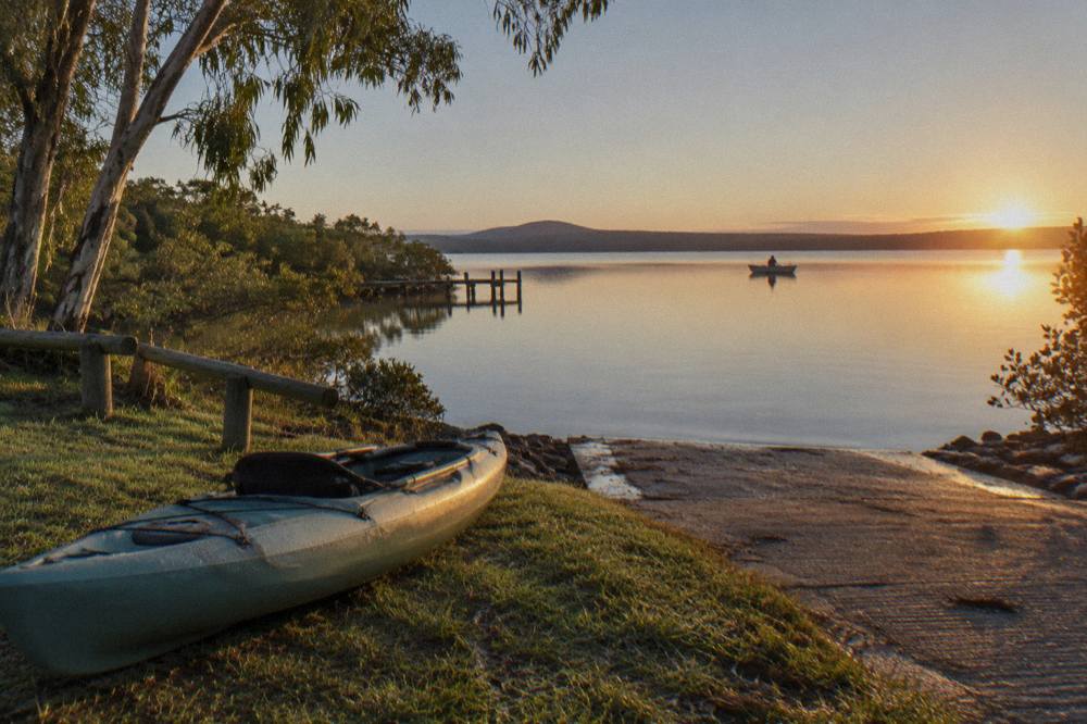 Kayaks lined up on a grassy launch bank beside a calm lake at early morning
