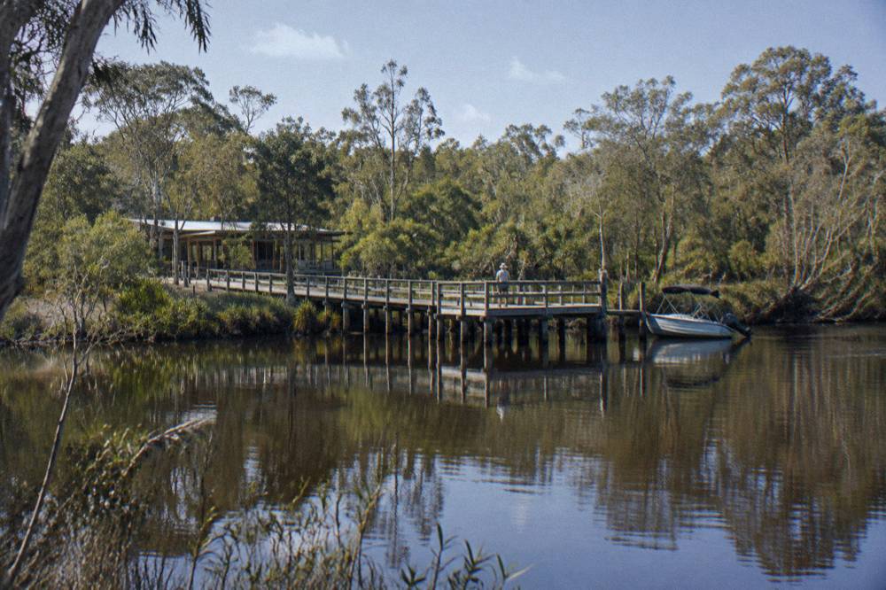 A timber boardwalk information centre surrounded by still dark water and reflected trees