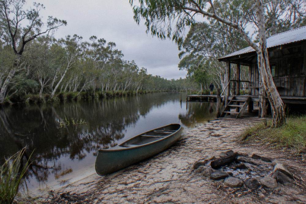 A lone canoe on a narrow river between tall paperbark trees with dark reflective water
