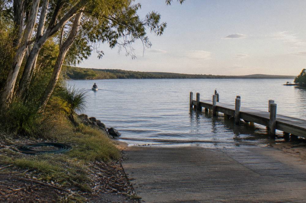 Boat ramp and jetty on a calm lakeshore with forest beyond in late afternoon light