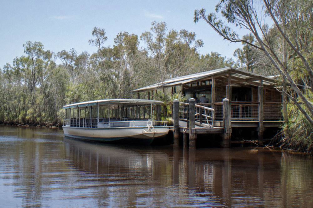 A small cruise boat moored at a jetty on a dark tannin river