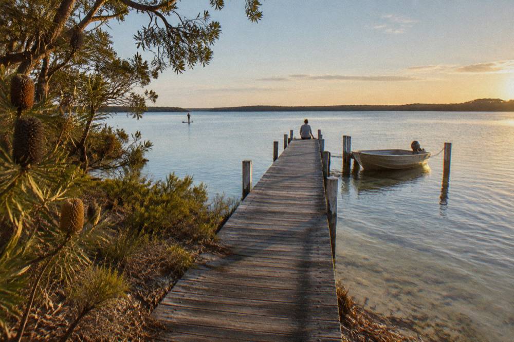 Wide calm lake with a wooden jetty extending into the water under a clear sky