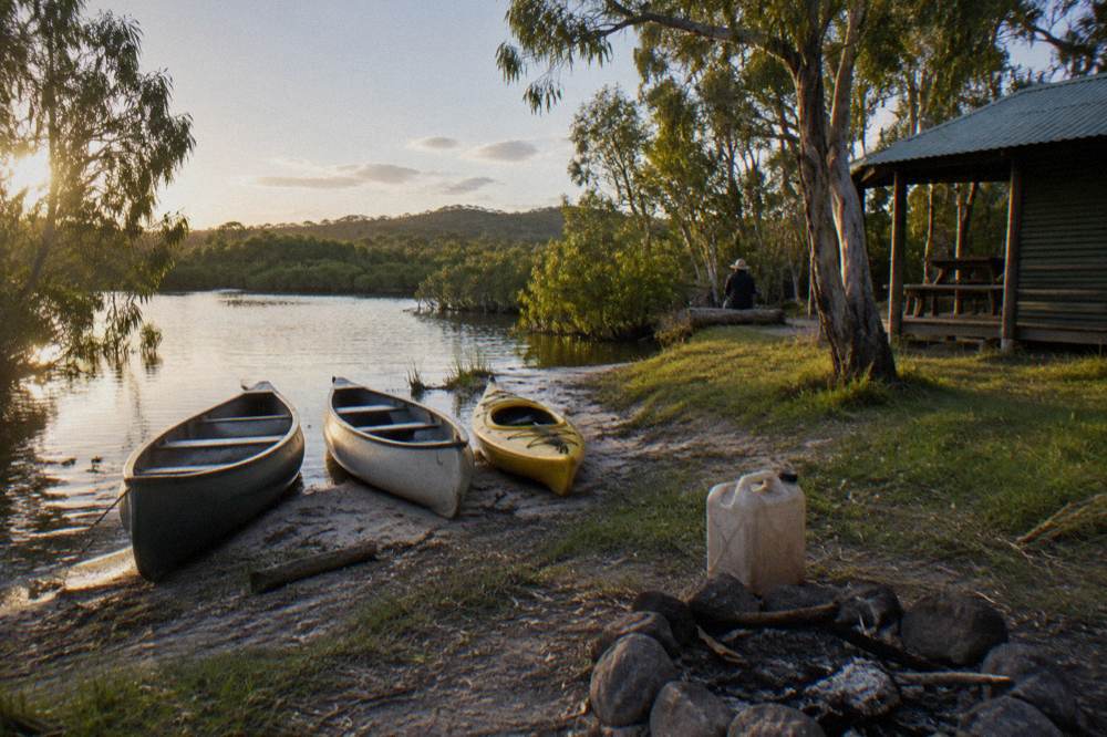 Canoes and kayaks pulled up on a grassy river bank beside calm water