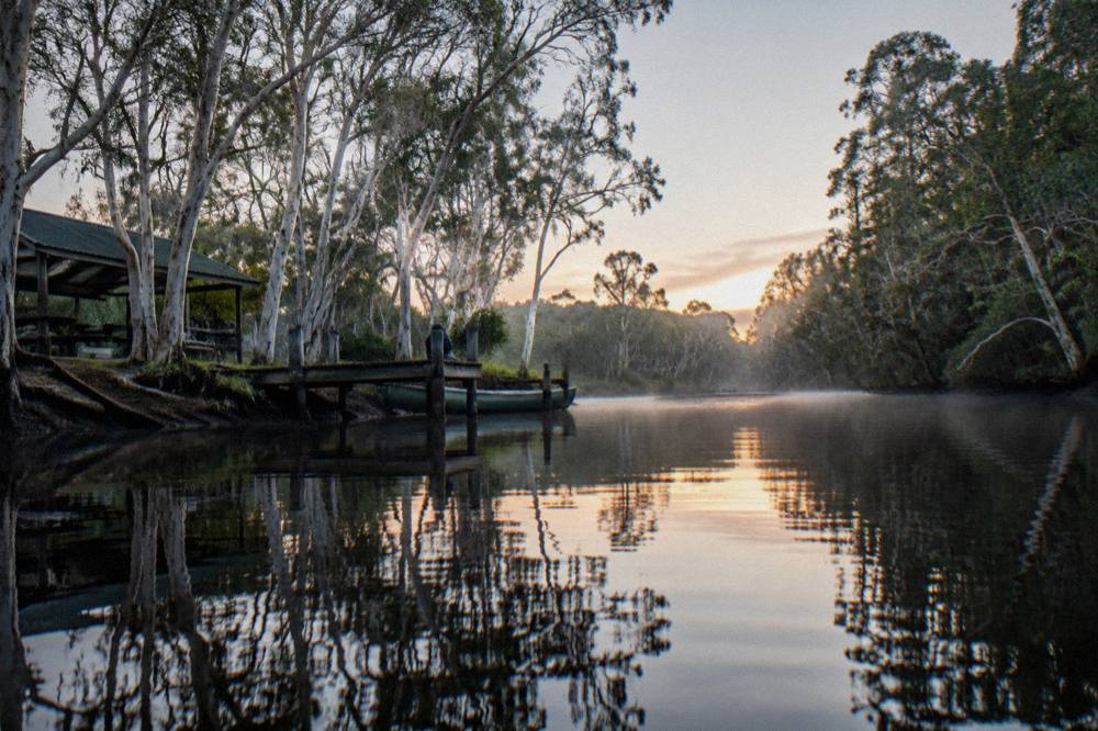 Still dark river water reflecting paperbark trees along the bank