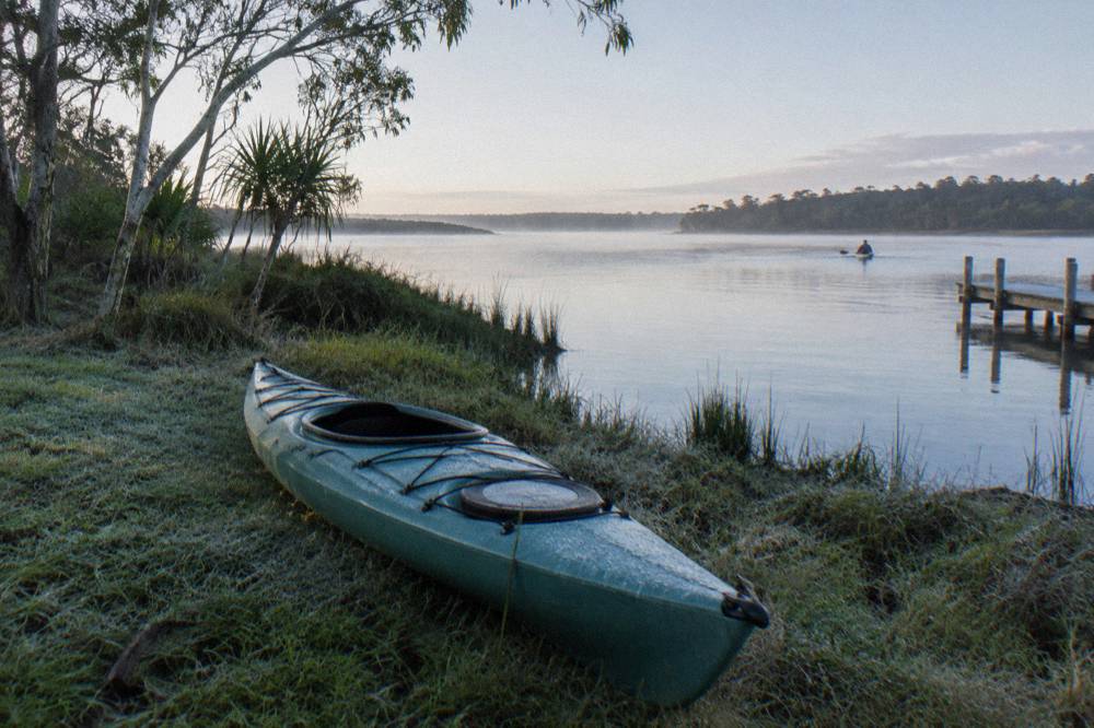 Kayak resting on a grassy bank beside a quiet river