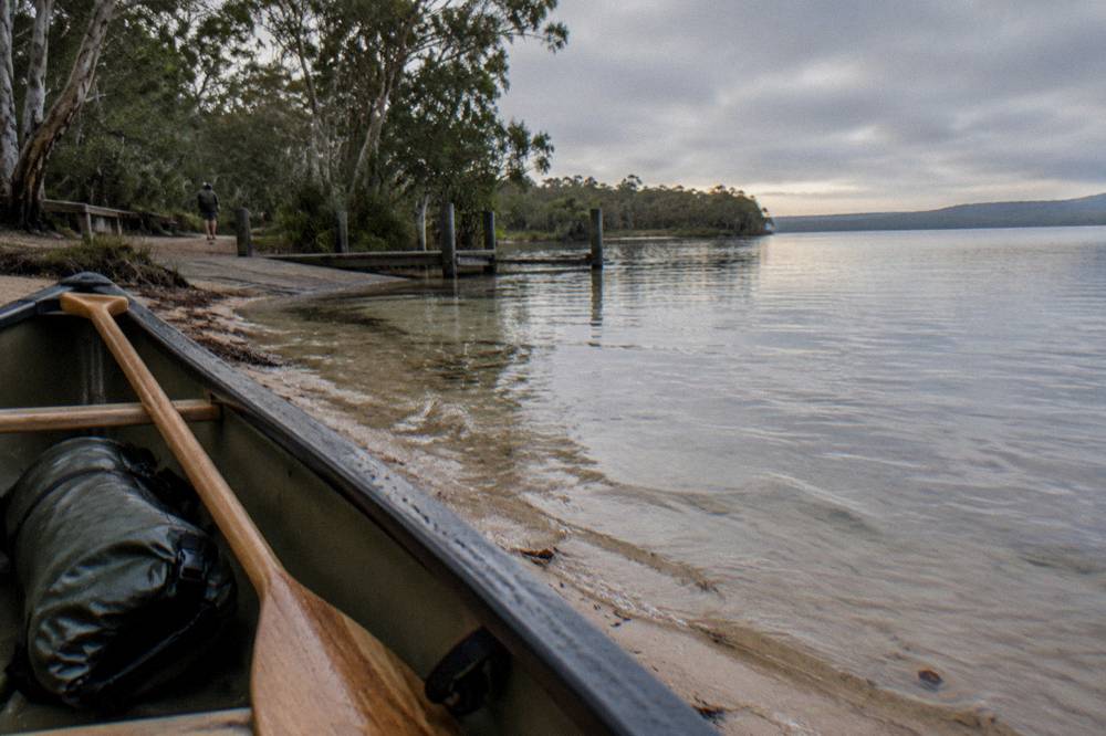 Dry bag and paddle resting in an open canoe at a river bank
