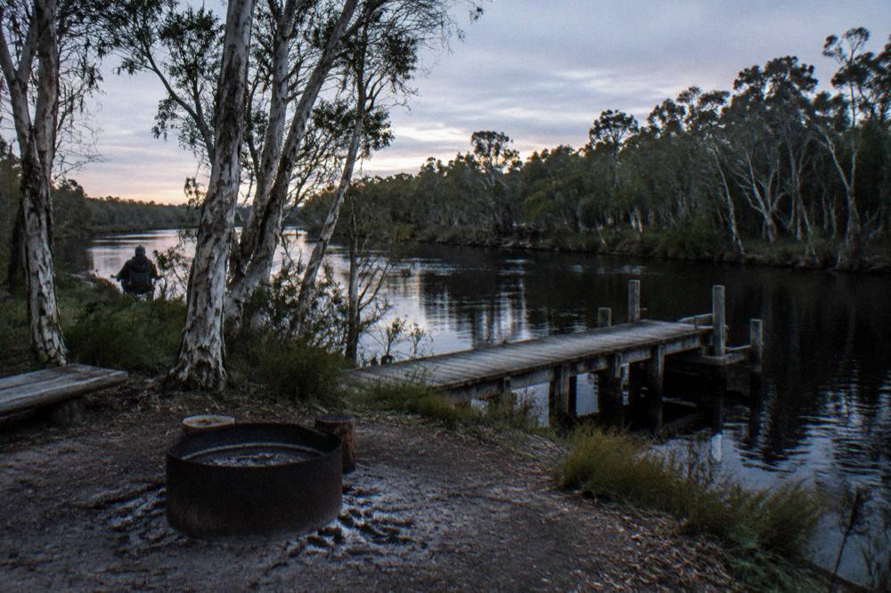 Timber jetty over dark calm river water at a camping area